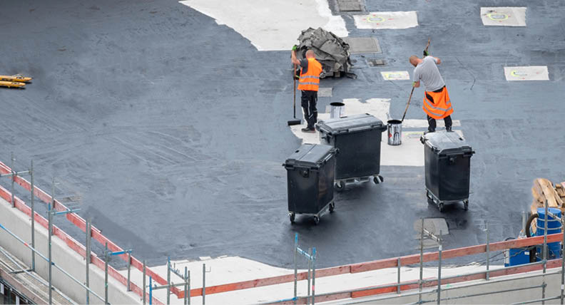 Roofer painting flat roof of a commercial building. 