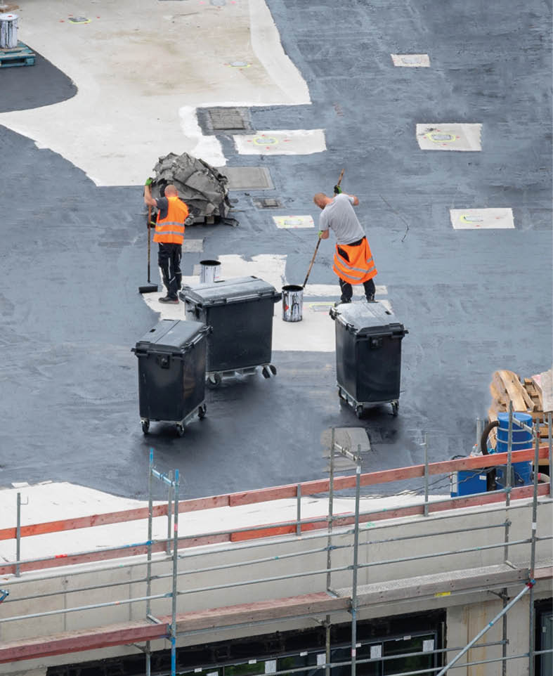 Roofer painting flat roof of a commercial building. 
