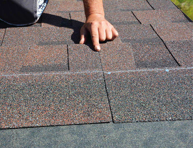 Asphalt roof shingles installation. A roofer is nailing bitumen, asphalt roofing shingles properly along the nailing line. 