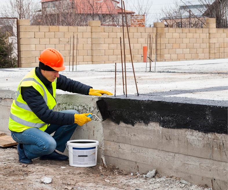 construction worker makes bituminous waterproofing of the foundation at the construction site